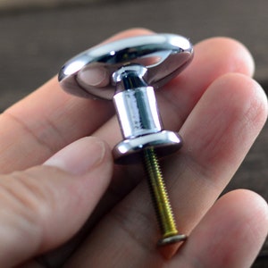 May include: A chrome cabinet knob with a round, slightly raised top and a screw for installation.
