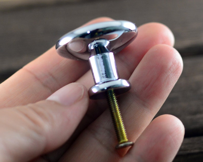 May include: A chrome cabinet knob with a round, slightly raised top and a screw for installation.