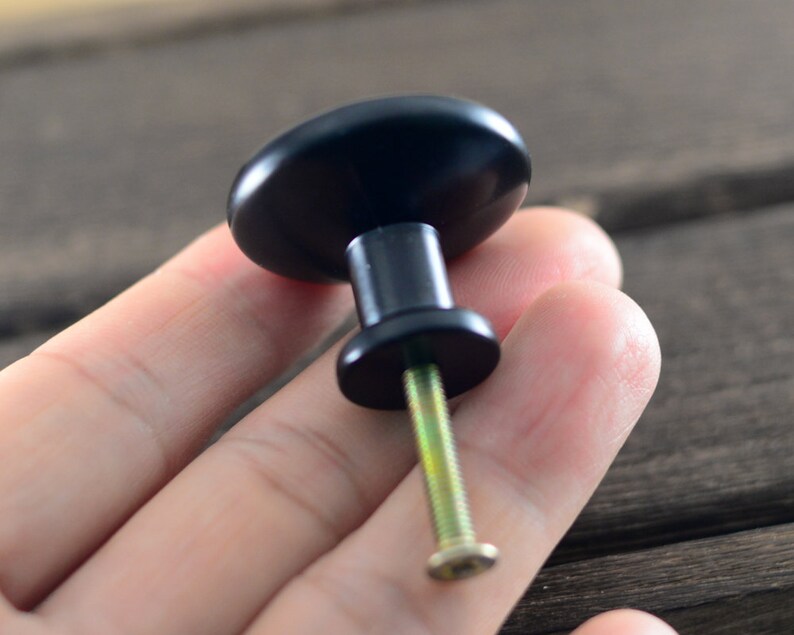 May include: Black cabinet knob with a round, smooth surface and a silver screw.