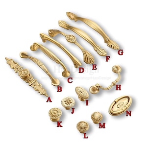 K&ouml;nnte beinhalten: Eine Sammlung goldfarbener Schrankbeschl&auml;ge, darunter Griffe und Kn&ouml;pfe. Die Griffe variieren im Design, mit verzierten und schlichten Stilen. Kn&ouml;pfe weisen florale und geometrische Muster auf. Die Beschl&auml;ge sind auf wei&szlig;em Hintergrund angeordnet.