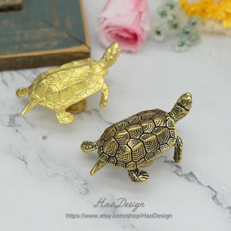 Peut inclure: Deux tirettes de tiroir en forme de tortue dor&eacute;es. Les tortues ont un design de carapace d&eacute;taill&eacute; et sont tourn&eacute;es vers la droite de l'image.