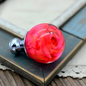 May include: A clear glass sphere with a pink rose inside. The sphere is attached to a silver metal base.