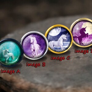 May include: Four round glass cabochons with silver and gold settings, each featuring a different image of a unicorn. The first image shows a white unicorn in a blue and green forest. The second image shows a white unicorn in a purple forest. The third image shows a white unicorn running on a beach with a full moon in the background. The fourth image shows a black silhouette of a unicorn running with a full moon in the background.