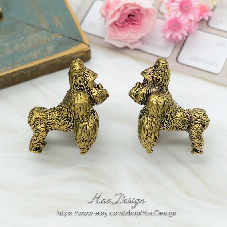 May include: Two gold-colored gorilla figurines facing each other. The figurines are detailed and have a textured surface. The figurines are on a white surface.