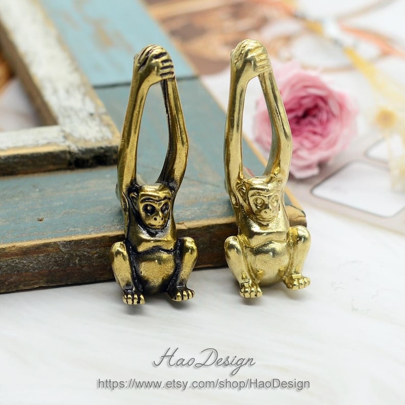 K&ouml;nnte beinhalten: Zwei goldene Affenfiguren mit erhobenen Armen. Die Affen sitzen auf einer Holzoberfl&auml;che.