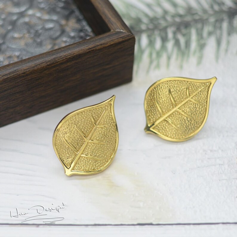 K&ouml;nnte beinhalten: Ein Paar goldene Ohrringe in Blattform. Die Ohrringe sind texturiert und haben ein zartes Design.