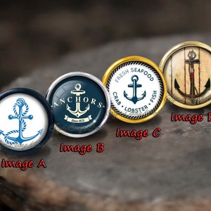 May include: Four round, decorative, glass cabochons with different nautical designs. The first cabochon has a white background with a blue anchor and rope. The second cabochon has a blue background with a white anchor and the text "ANCHORS Since 1873". The third cabochon has a gold rim and a white background with a blue anchor and the text "FRESH SEAFOOD CRAB LOBSTER FISH". The fourth cabochon has a wood-grain background with a red and white anchor.
