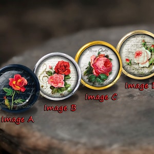Op de afbeelding: Vier ronde, decoratieve glazen cabochons met verschillende bloemmotieven. Elk cabochon is ingevat in een metalen frame. De ontwerpen omvatten een rode roos met een muzieknoten, een roze roos met de tekst "Mon Cheri", een witte roos met de tekst "Quitter le terrain" en een rode roos met een handgeschreven notitie.