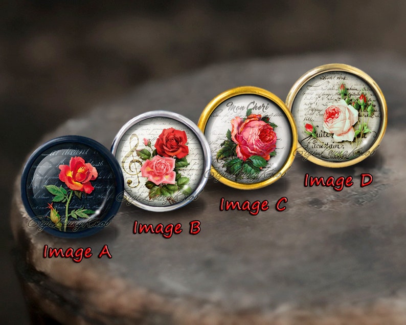 May include: Four round, decorative, glass cabochons with different floral designs. Each cabochon is set in a metal frame. The designs include a red rose with a musical note, a pink rose with the text "Mon Cheri", a white rose with the text "Quitter le terrain", and a red rose with a handwritten note.