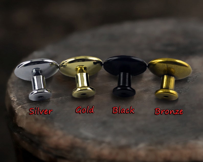 May include: Four oval-shaped metal knobs in silver, gold, black, and bronze. Each knob has a small round post.