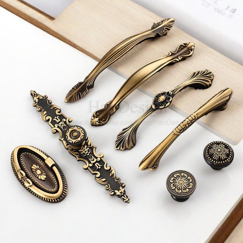 以下が含まれることがあります： アンティーク真鍮製のキャビネット金具の品揃え。取っ手とノブが含まれています。取っ手は様々なサイズとデザインで、装飾的なディテールと温かみのあるエイジング仕上げが施されています。ノブは花の模様が特徴です。