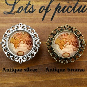 Op de afbeelding: Twee broches in antieke stijl met een wereldkaartontwerp. De broche aan de linkerkant is zilver en de broche aan de rechterkant is brons.