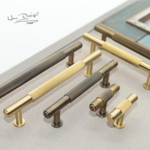 May include: Assortment of gold and bronze cabinet hardware with a ribbed design. The hardware includes pulls and knobs in various sizes.