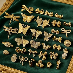 Può includere: Una collezione di spille e spille decorative in metallo color oro, tra cui farfalle, fiocchi, libellule e altre forme. Le spille sono disposte su una superficie di velluto verde scuro all'interno di una cornice color oro.