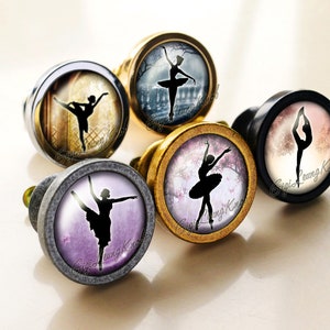 Può includere: Cinque pomelli rotondi per armadi con una silhouette di ballerina in varie pose su uno sfondo bianco. Ogni pomello ha un colore di sfondo e un design diversi. I pomelli sono in metallo con una finitura argentata, dorata o nera.