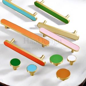 May include: A collection of colorful cabinet hardware, including long bar pulls and round knobs. The pulls feature gold-toned metal with vibrant accents in blue, green, orange, and pink. The knobs have matching colors. The Etsy shop name is visible.
