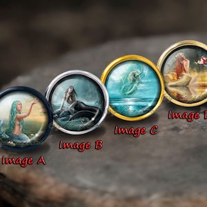 May include: Four round glass cabochons with gold settings, each featuring a different mermaid illustration. The mermaids are depicted in various poses and settings, including a mermaid with a fish, a mermaid swimming in the ocean, a mermaid with a crown, and a mermaid with a dark background.