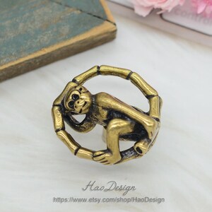 Puede incluir: Pomo de armario de mono dorado con un dise&ntilde;o de bamb&uacute; circular. El mono se agarra al bamb&uacute; y mira hacia un lado.