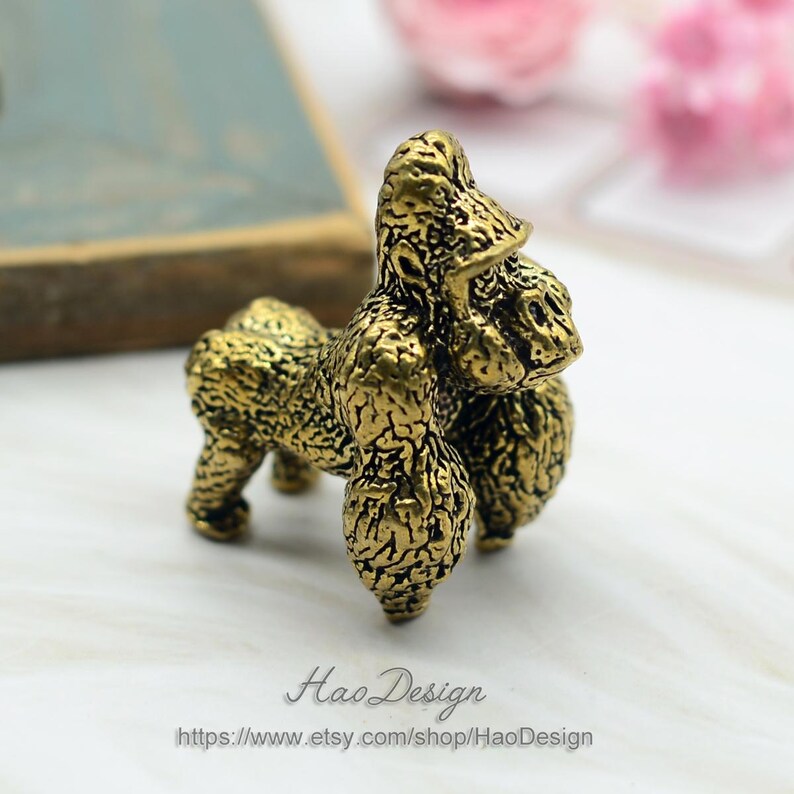 May include: A small, gold-colored, detailed figurine of a gorilla. The figurine is standing on a white surface.