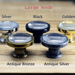 以下が含まれることがあります： 透明なガラスのトップと金属製のベースを持つ5つのキャビネットノブ。ノブの色はシルバー、ブラック、ゴールド、アンティークブロンズ、アンティークシルバーです。