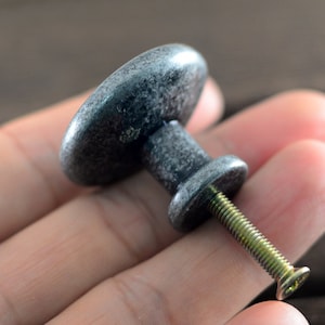 May include: A silver-toned metal cabinet knob with a round, slightly oval-shaped top and a screw. The knob has a distressed finish.