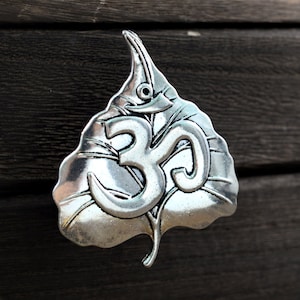 May include: A silver pendant shaped like a leaf with an Om symbol in the center.