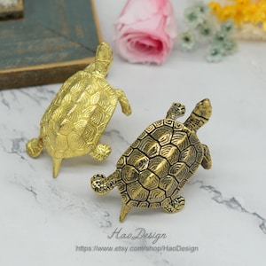 Peut inclure: Deux figurines de tortues dor&eacute;es avec des motifs de carapace d&eacute;taill&eacute;s. Les tortues sont tourn&eacute;es dans des directions diff&eacute;rentes et sont faites d'un m&eacute;tal brillant.