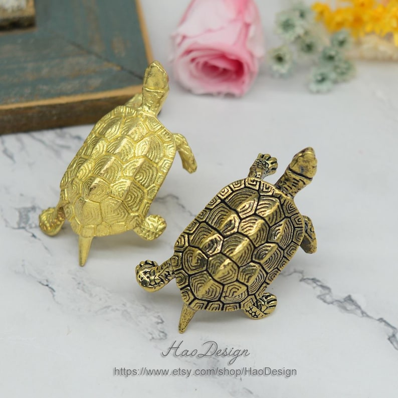 Peut inclure: Deux figurines de tortues dor&eacute;es avec des motifs de carapace d&eacute;taill&eacute;s. Les tortues sont tourn&eacute;es dans des directions diff&eacute;rentes et sont faites d'un m&eacute;tal brillant.
