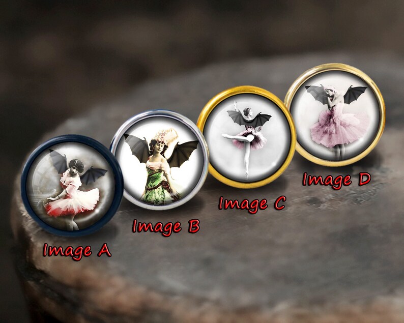 K&ouml;nnte beinhalten: Vier runde, dekorative Metallkn&ouml;pfe mit Bildern von Frauen mit Fledermausfl&uuml;geln, die T&uuml;llr&ouml;cke tragen. Die Kn&ouml;pfe sind mit A, B, C und D beschriftet.