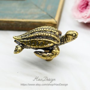 Op de afbeelding: Een gouden metalen schildpadfiguur met een gedetailleerde schelp en een gestructureerd oppervlak. De schildpad bevindt zich in een zwempositie met zijn kop omhoog en zijn poten gestrekt.