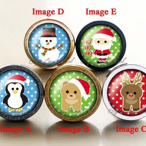 May include: Five round Christmas themed cabinet knobs with different designs. The knobs are made of metal with a silver, gold, or black finish. The designs include a penguin, a bear, a reindeer, a snowman, and Santa Claus.