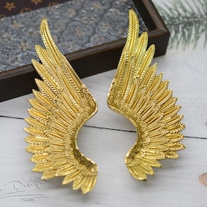 Peut inclure: Deux ailes d'ange en métal couleur or avec un design de plumes détaillé. Les ailes sont légèrement incurvées et ont une surface texturée.
