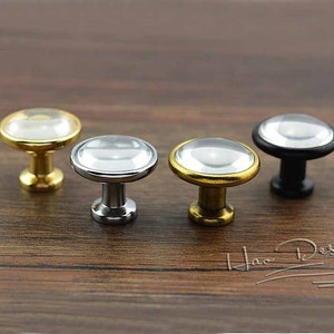 May include: Four cabinet knobs with a clear glass top and a metal base. The knobs are in gold, silver, and black.