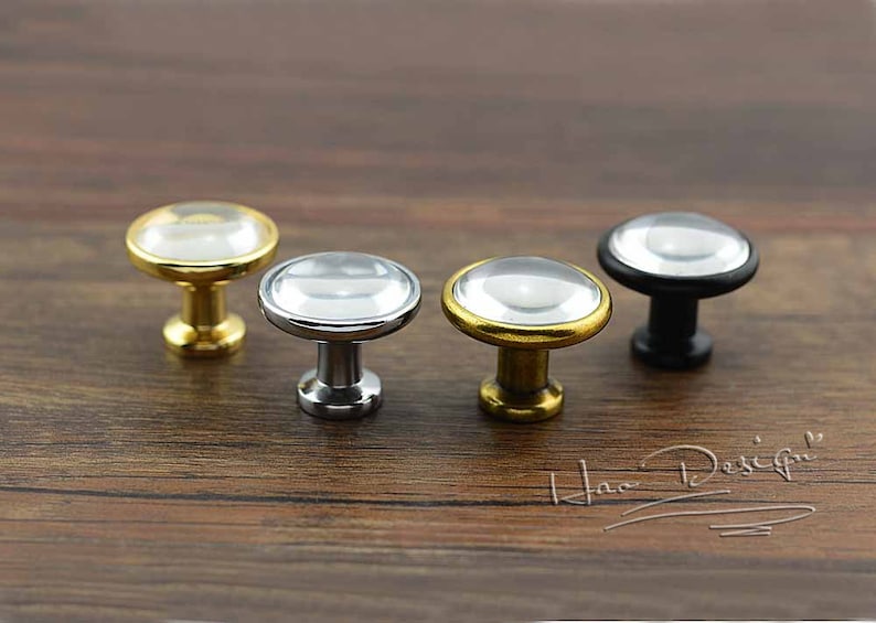 May include: Four cabinet knobs with a clear glass top and a metal base. The knobs are in gold, silver, and black.