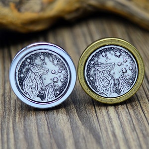 May include: Two silver and gold tone metal cufflinks featuring a design of two wolves howling at the moon with stars in the background.