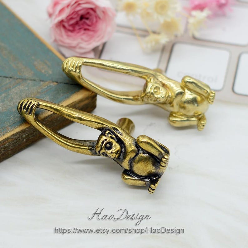 K&ouml;nnte beinhalten: Zwei goldene, detailreiche Schrankkn&ouml;pfe in Affenform. Die Affen sitzen mit erhobenen Armen.