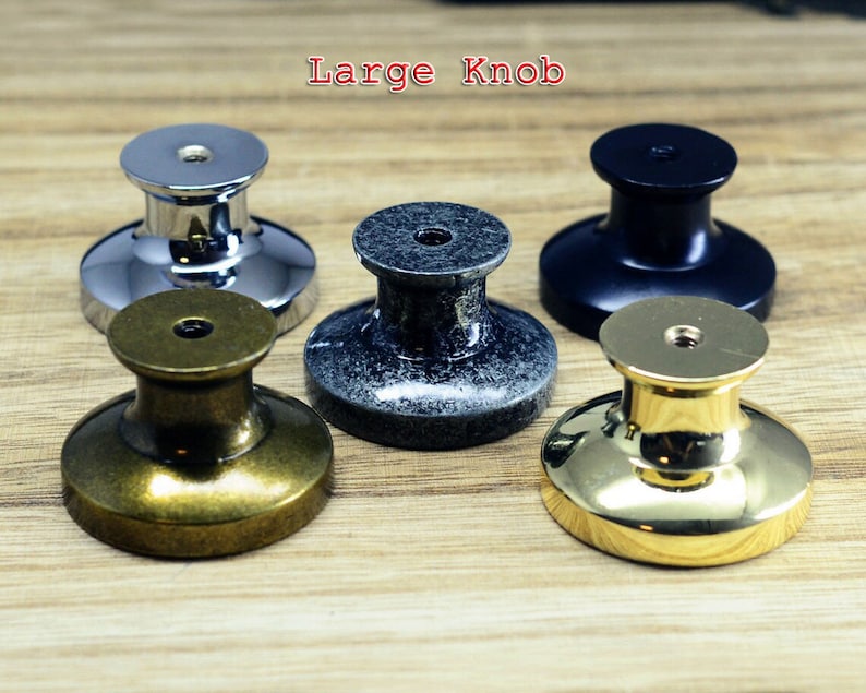 以下が含まれることがあります： 5つの異なる仕上げのキャビネットノブ: 光沢のあるクロム、アンティークブラス、ブラック、2色のグレー。ノブは丸型で、中央が盛り上がり、ベースはフラットです。画像の上部に「Large Knob」というテキストが表示されています。