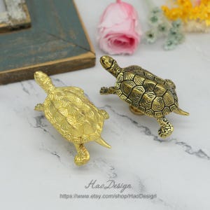 Peut inclure: Deux tirettes de tiroir en forme de tortue de couleur dor&eacute;e. Les tortues sont d&eacute;taill&eacute;es avec des carapaces textur&eacute;es et ont une finition l&eacute;g&egrave;rement diff&eacute;rente.