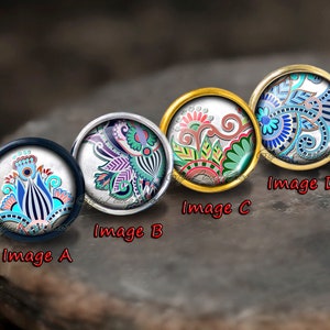 May include: Four round decorative buttons with intricate floral designs. Each button features a different color scheme: blue, purple, red, and blue. The buttons have silver and gold-colored metal rims. The image is labeled with the letters A, B, C, and D.