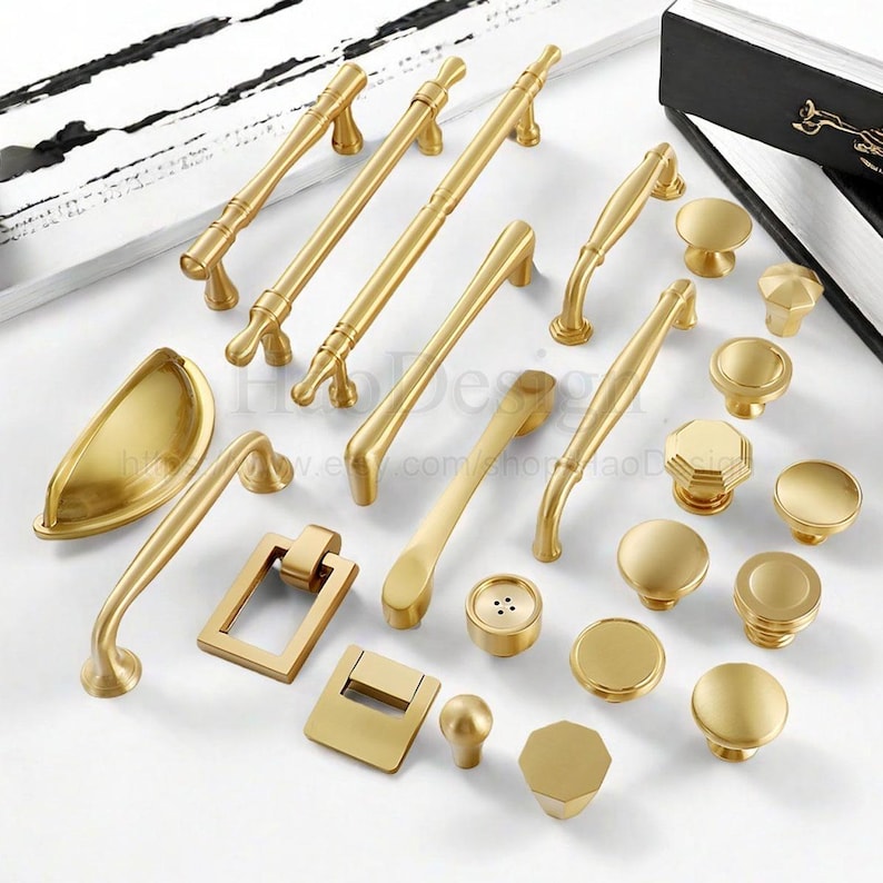 May include: A collection of gold-colored cabinet hardware, including handles, knobs, and pulls. The hardware features various designs, from simple to ornate, with a matte finish. The assortment includes different shapes and sizes for diverse furniture applications.