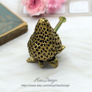 Op de afbeelding: Gouden metalen kastknop in de vorm van een aardbei met een getextureerd oppervlak en een schroef voor installatie.