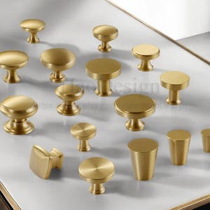 Puede incluir: Una colecci&oacute;n de pomos y tiradores dorados para armarios de varias formas. Los pomos presentan dise&ntilde;os redondos, cuadrados y cil&iacute;ndricos. Algunos tienen forma de hongo, mientras que otros son m&aacute;s minimalistas.