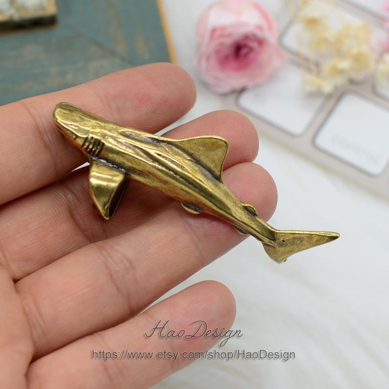 May include: A gold-colored metal shark figurine. The shark is detailed with fins and scales. The figurine is about 3 inches long.