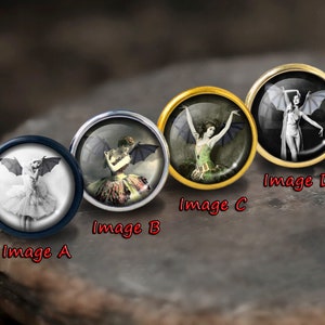 Può includere: Quattro bottoni rotondi decorativi con immagini di donne con ali di pipistrello. I bottoni sono di diversi colori e hanno un bordo dorato, argentato o blu.