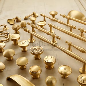 May include: A collection of various brass cabinet hardware, including knobs and pulls. The hardware features a range of designs, from simple round knobs to ornate pulls with decorative detailing. The brass finish gives the hardware a warm, classic look.