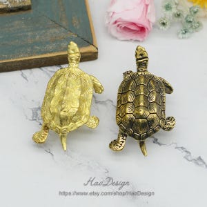 Peut inclure: Deux figurines de tortues dor&eacute;es avec des motifs de carapace d&eacute;taill&eacute;s. La tortue &agrave; gauche est brillante et la tortue &agrave; droite a une finition plus antique.