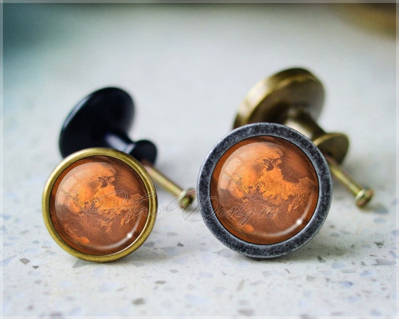 May include: Two cabinet knobs with a bronze finish and a round, gray metal base. The knobs feature a circular image of Mars, a reddish-brown planet with visible surface features.
