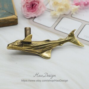 May include: A brass shark fin shaped drawer pull with a textured surface. The pull is mounted on a white surface.  Hao Design https://www.etsy.com/shop/HaoDesign