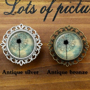 May include: Two dandelion brooches, one in antique silver and one in antique bronze. Both brooches feature a glass cabochon with a vintage-style image of a dandelion.