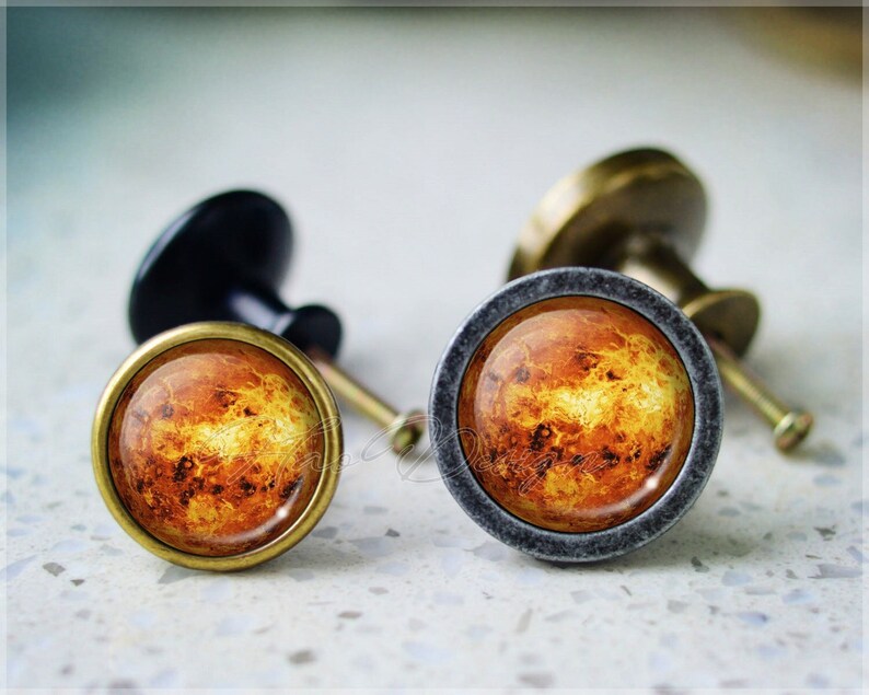 Peut inclure: Deux boutons de porte ronds avec une base en laiton et un dessus en verre repr&eacute;sentant une image d&eacute;taill&eacute;e de la plan&egrave;te Jupiter. Le bouton de gauche a une bordure en laiton, tandis que le bouton de droite a une bordure grise.